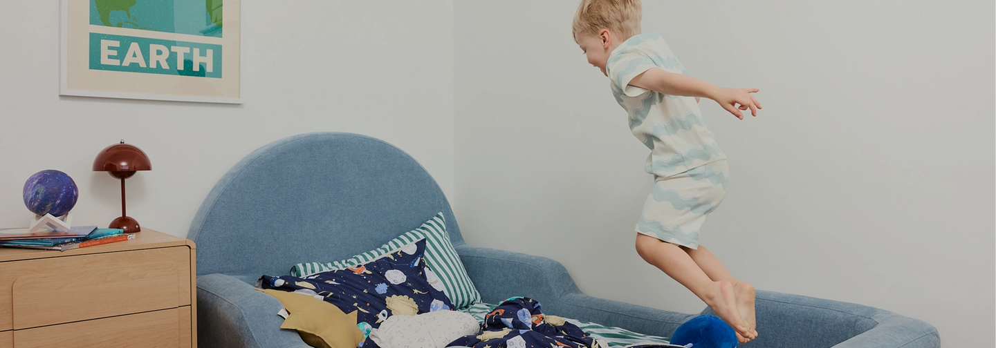 Child jumping on a blue couch in a room with a 'Earth' poster on the wall.